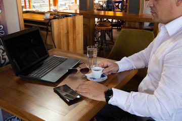 A bussnisman sitting in restaurant working on lap top and drink coffee 