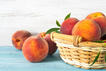 sweet ripe juicy fruit, peaches with green leaves in basket on blue wooden background