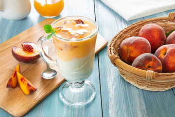 Glass of yogurt with slices of sweet ripe juicy fruit, peaches with green leaves in a basket on white background