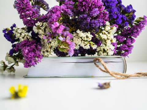 Bouquet of dried flowers lies on a closed book in which the bookmark. Separately lie fallen off flowers
