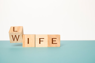 Flipping one wooden cube to change the word Life to Wife on neutral background