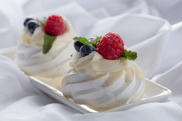 Dessert Pavlova with raspberries, blueberries and mint on a white fabric.
