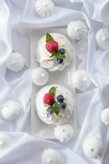 Dessert Pavlova with raspberries, blueberries and mint on a white fabric.