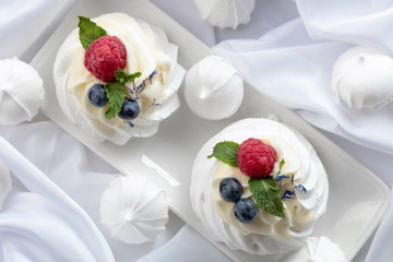 Dessert Pavlova with raspberries, blueberries and mint on a white fabric.