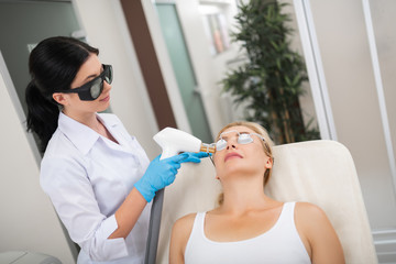 Smiling cosmetologist making her client laser procedure.