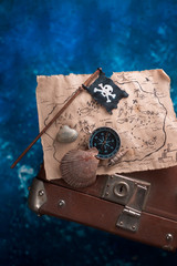 Treasure map with seashells and Jolly Roger on a suitcase. Ready to go for an adventure flat lay with copy space.