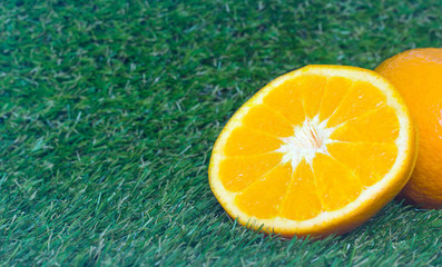 Full orange fruit and half cut on green grass.