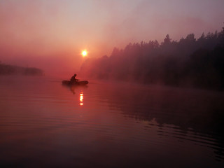 Fishing at dawn. Silhouette of a fisherman in a boat in the fog at sunrise.