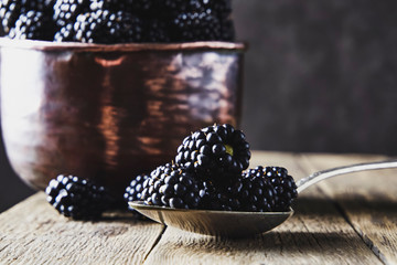 Ripe blackberries in old copper dishes on old wooden boards and lying next to a spoon on a dark background.