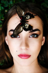 Portrait of beautiful young girl with butterfly sitting on her face. Big black butterfly Papilio lowi sat on the woman's forehead