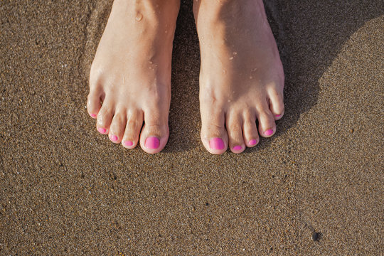 Top view of two female feet isolated on sunny wet sand of seashore. Happy woman enjoy summer vacations and warm sea water at  tropical resort. Fingernails with fresh professional pink pedicure.