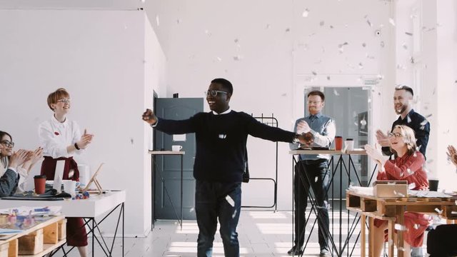 RED EPIC-W Happy young African businessman celebrating success dancing with confetti and team at office slow motion.
