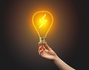 Hand holding light bulb on dark background. New Eco idea concept
