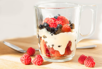 fresh ripe organic berries (blueberries and raspberries) with cream (yogurt) in a glass cup, side view