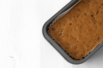 Fruit cake loaf mixture in a metal baking tin.  On a white wood background