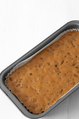 Fruit cake loaf mixture in a metal baking tin.  On a white wood background