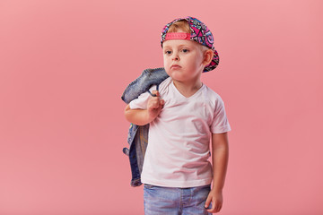 Little serious fashionable toddler boy in denim clothes and trendy cap. Isolated on pink background © oes