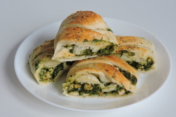 A stromboli pizza with spinach, chicken, feta, mushrooms served on a white plate, white background