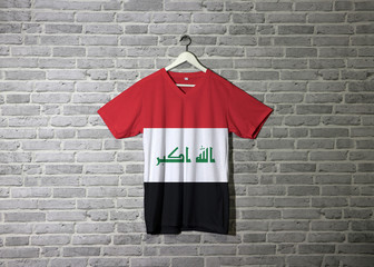 Iraq flag on shirt and hanging on the wall with brick pattern wallpaper.