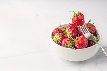 Fresh organic strawberry in the white bowl and fork, on the white background.