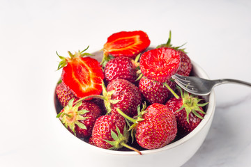 Fresh organic strawberry in the white bowl and fork, on the white background.