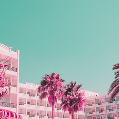 Palms and plants on background of hotels. Minimal and bright. Infrared pink and turquoise sky style