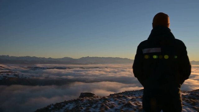 The silhouette of a man stands at sunset above the clouds and contemplates the setting sun. The concept of tranquility and pleasure in traveling