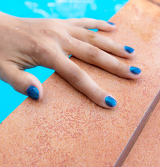 Hands of a girl with blue manicure in the water of the pool