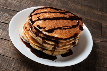 Heap of homemade pancakes with chocolate cream lies on round white ceramic plate and old rustic wooden table