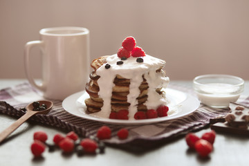 Pancakes on dark wooden table decorated with berries, spoon, cup with coffee or tea, raspberry and blueberry, tasty breakfast for family, healthy eating concept, composition over dark surface.