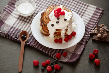 Delicious breackfast for family, pancackes with sour cream and berries, kitchen table decorated with raspberries, blueberries, wooden spoon, white palte with muffns, chocholate pieces. Food concept.