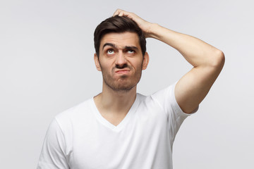 Young man thinking, scratching his head trying to find solution, isolated on gray background