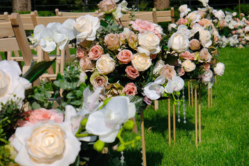 Floral bouquets and white wooden empty chairs on green grass. Wedding ceremony decorations.