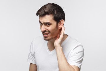 Young man pressing hand to ear trying to hear something better isolated on gray background