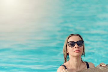 Young woman in sunglasses relaxing in swimming pool on summer vacation.