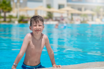 Happy smiling Caucasian boy having fun in swimming pool at resort on summer vacations