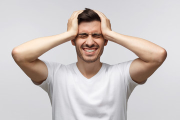 Young man pressing hands to temples experiencing bad headache, having shut eyes because of pain,...