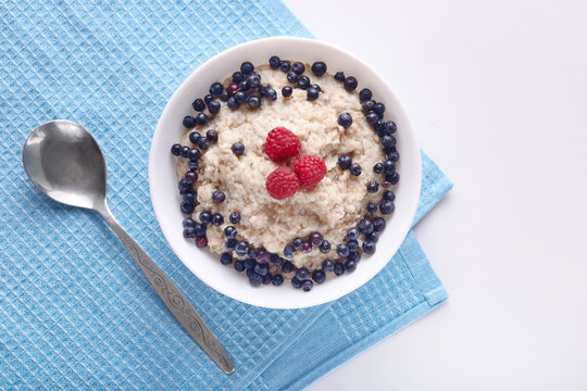 Image of bowl of oatmeal porridge with blueberries and raspberries on white wooden table, tasty english brekfast, delicious meal for healthy eater isolated on white. Halthy eating and diet concept.