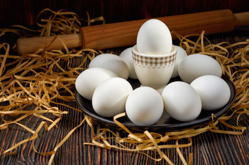 White eggs on a black plate, paper straw and wooden table. On the back of the rolling pin. Restrained.
