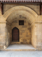Wooden grunge door and window covered with interleaved wooden grid in recessed stone bricks wall at facade of caravansary - Wikala of Bazaraa, suited in Gamalia district, Medieval Cairo, Egypt