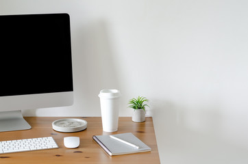 Modern personal computer screen on wooden table with a cup of coffee and Tillandsia air plant with space for text on white wall for working and office concept.