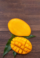 Fresh mango - beautiful chopped fruit with green leaves on dark wooden timber background. Tropical fruit design concept. Flat lay. Top view. Copy space