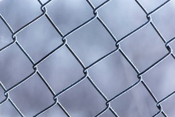 Close up view of Frozen metal fence frost covered in cloudy winter day. Soft focus