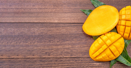 Fresh mango - beautiful chopped fruit with green leaves on dark wooden timber background. Tropical fruit design concept. Flat lay. Top view. Copy space