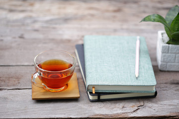 Red tea in transparent glass with notebooks and pencil and plant pot on rustic wooden table
