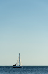Summer day on the Adriatic sea.  In the distance, a white sailboat is sailing along the sea in the...