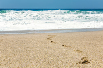Footprints on the sandy shore of the turquoise sea. Clear sunny day. blue sky. Space for text.