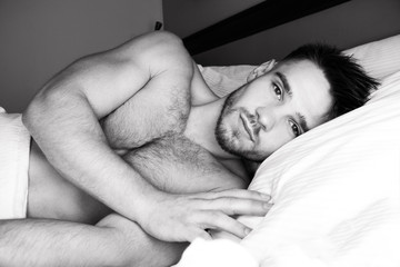 Good looking naked man lying in between white sheets