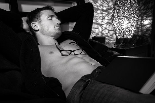 Sexy man with open shirt sleeping on bed with book and glasses resting on his body