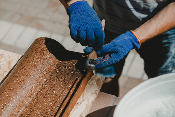 Gloved hands paint shingles with brush